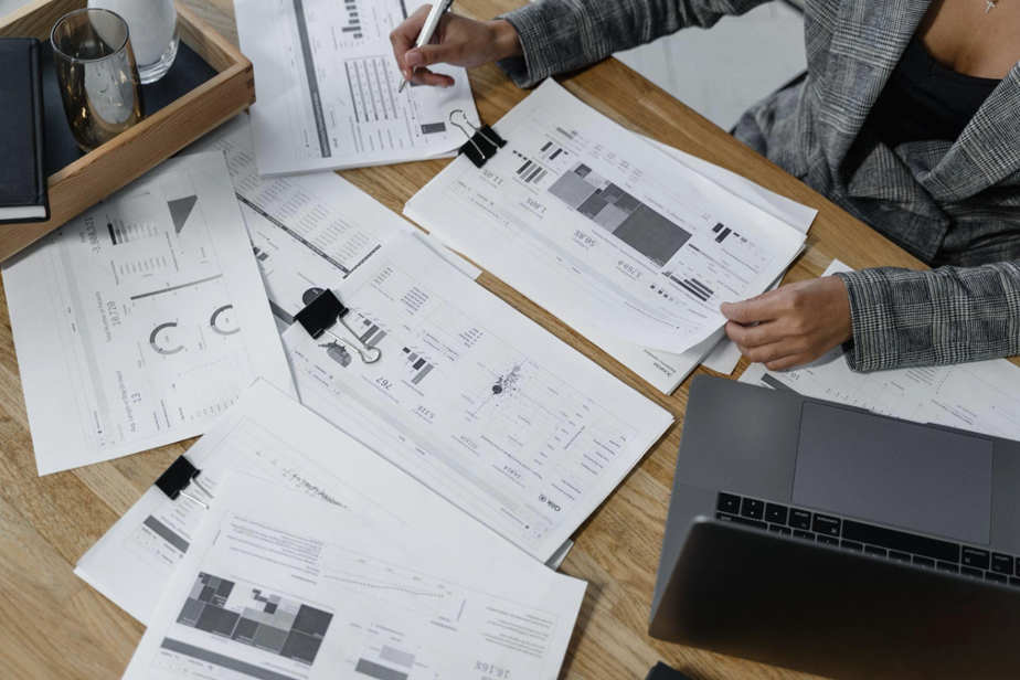 A woman at a desk with a laptop and documents spread out all over it. 