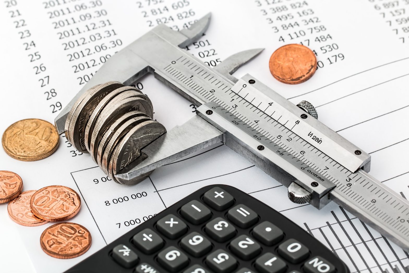 A wrench pinching coins next to a calculator on a sheet showing expenses for a business.