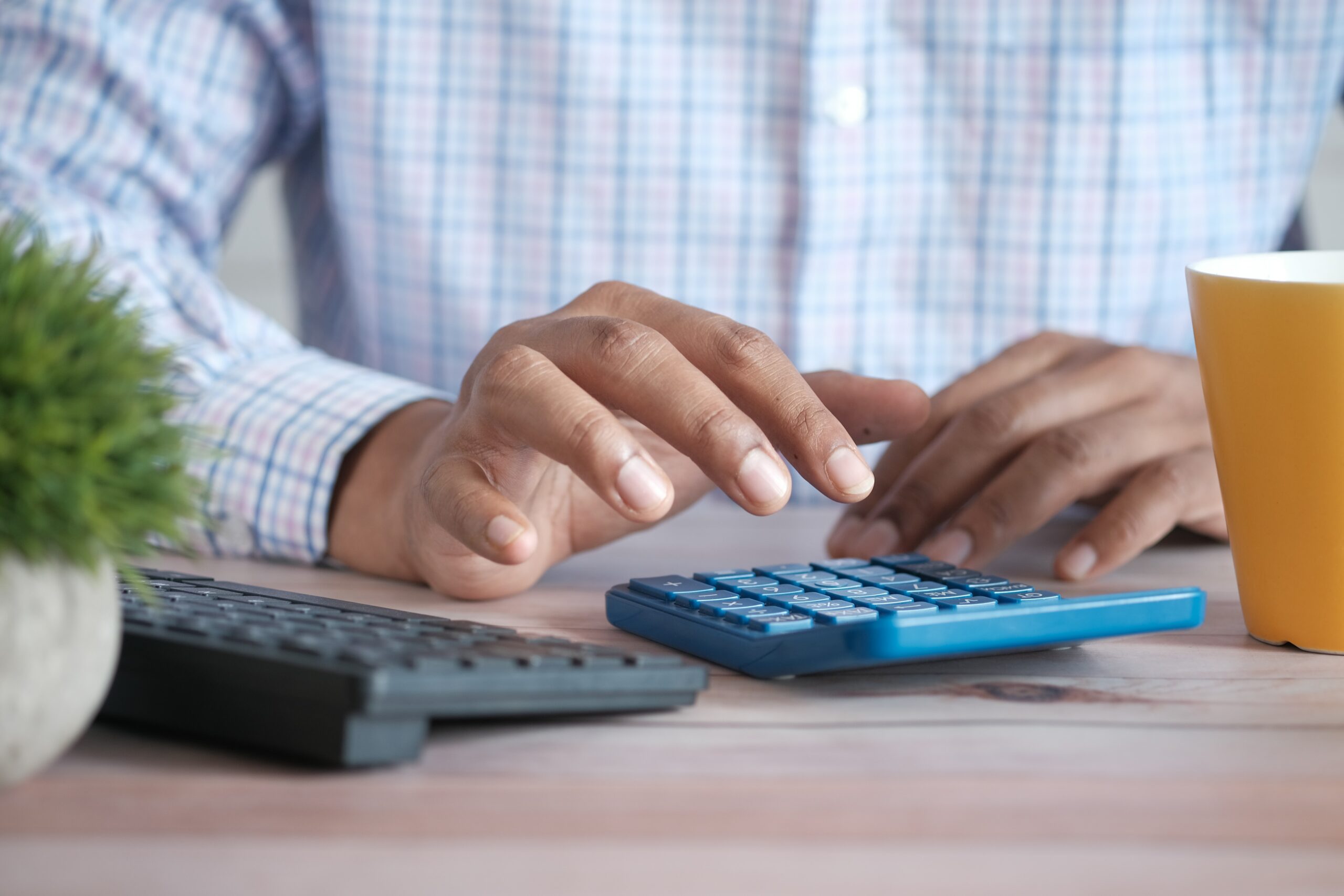 A man punching keys on a calculator next to a keyboard.
