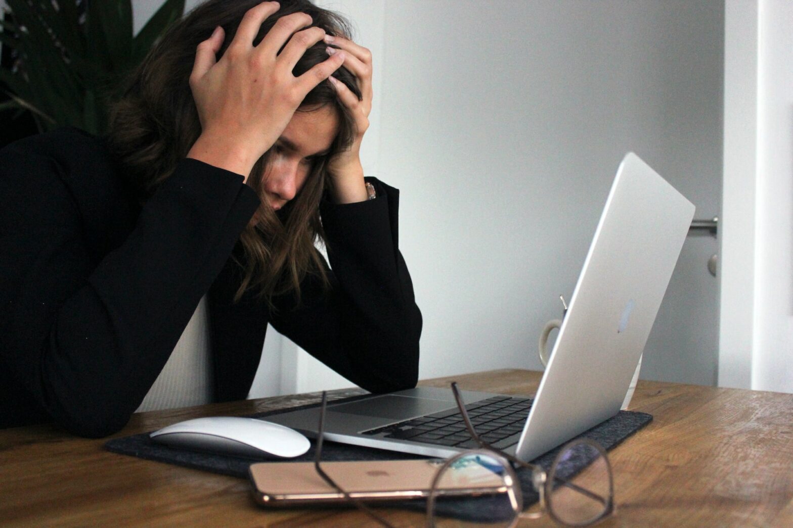 A woman sitting in front of a laptop with her head in her hands in a frustrated posture.