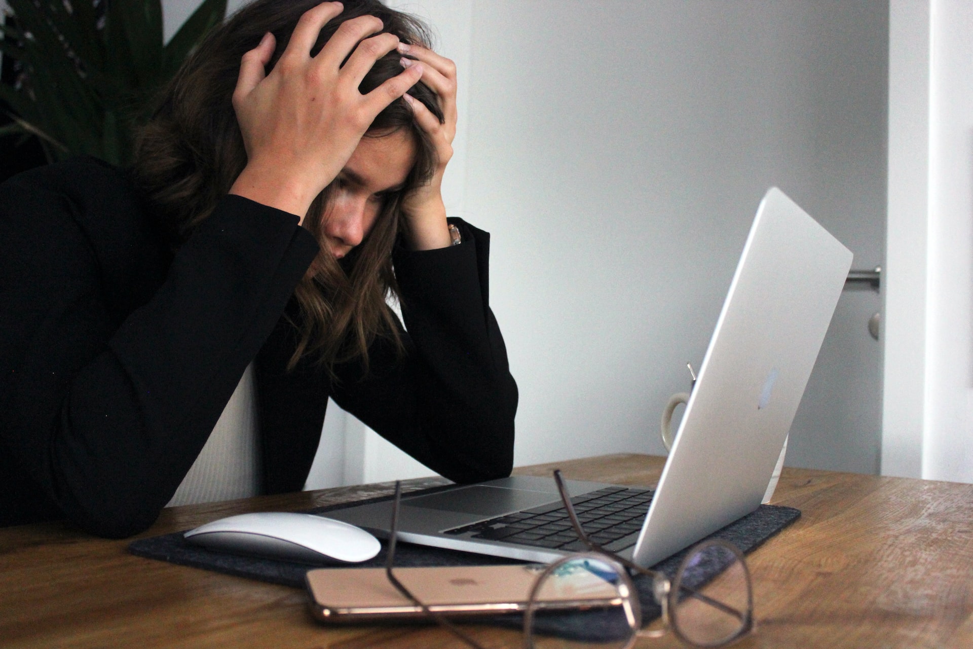 A woman sitting in front of a laptop with her head in her hands in a frustrated posture.