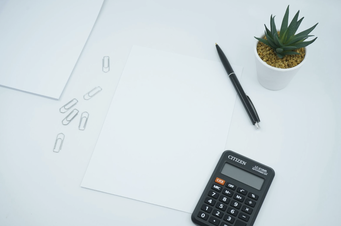 A calculator, pen, and paperclips on a sheet of paper.