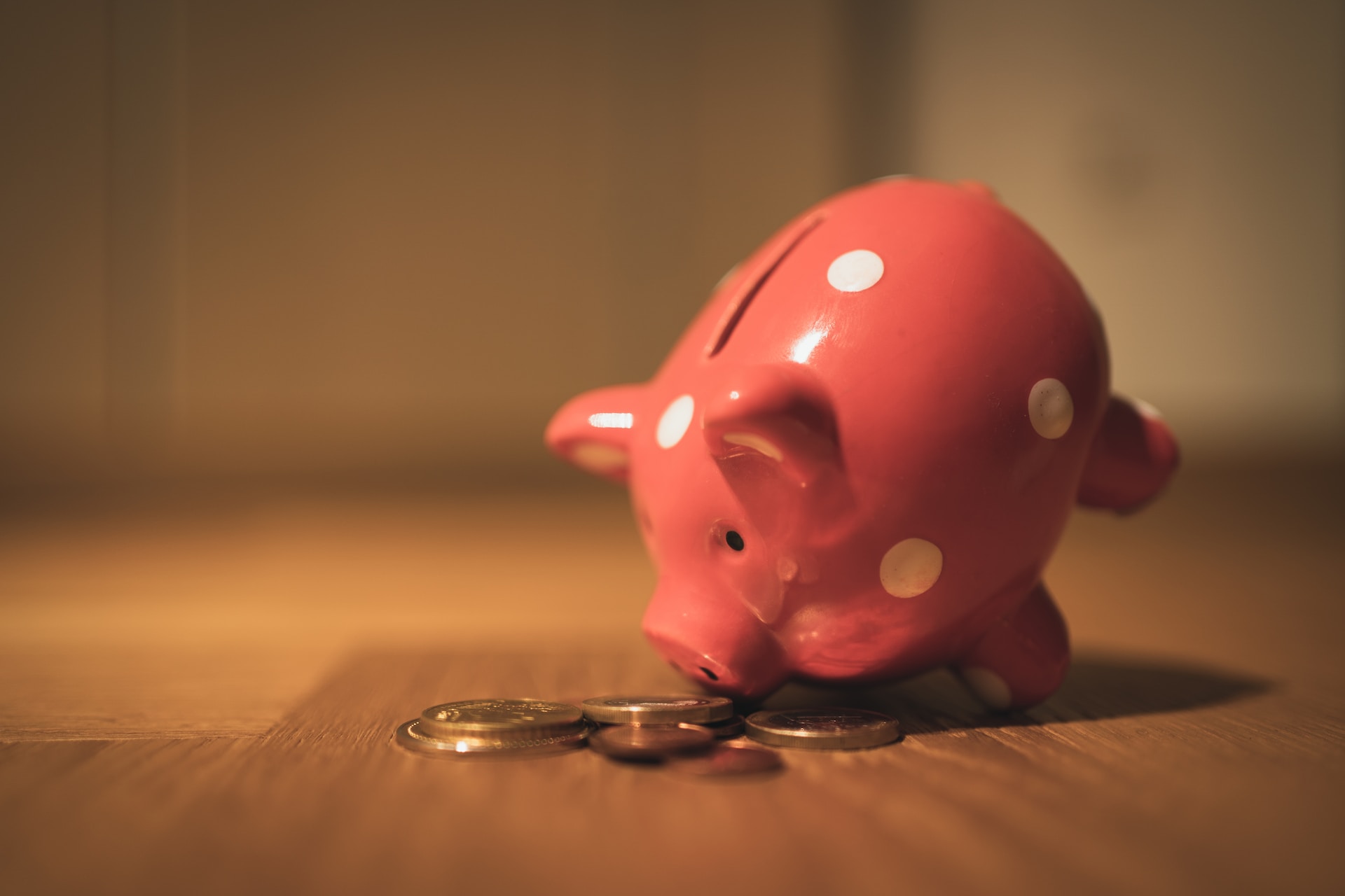 A pink piggy bank next to some coins. 