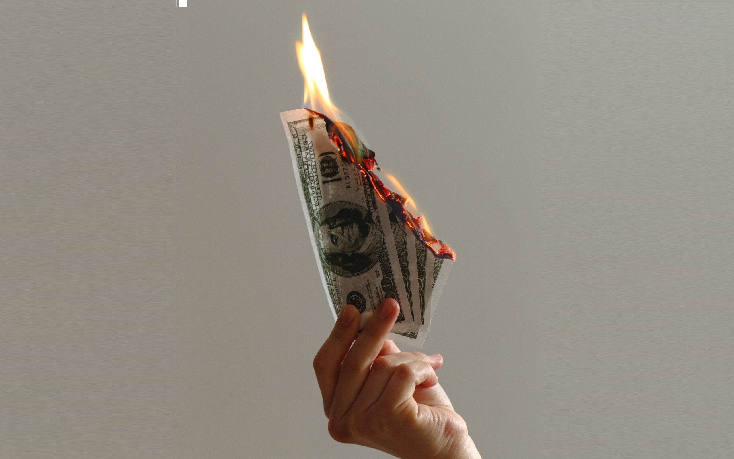 A hand holding burning dollar bills.