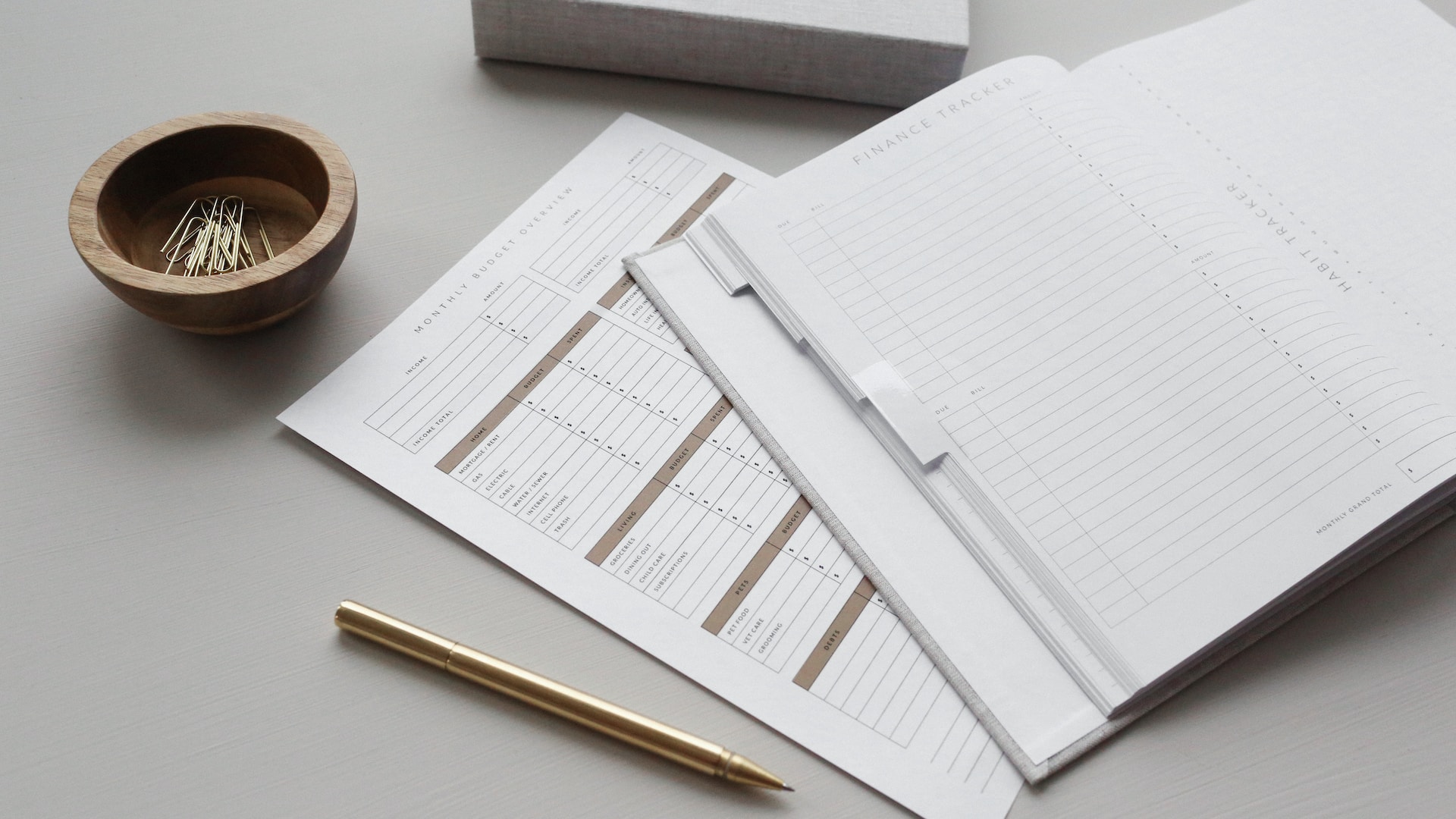 A blank notebook on a table with a heading that reads "Finance Tracker" next to a loose sheet of paper and a pencil.