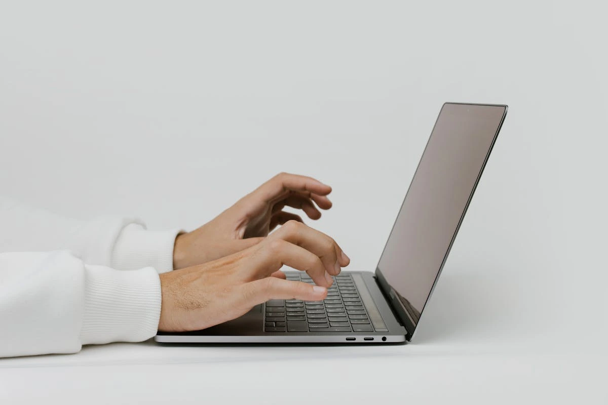 Detailed view of a man's hands engaged in typing on a laptop, showcasing the fingers positioned over the keys.