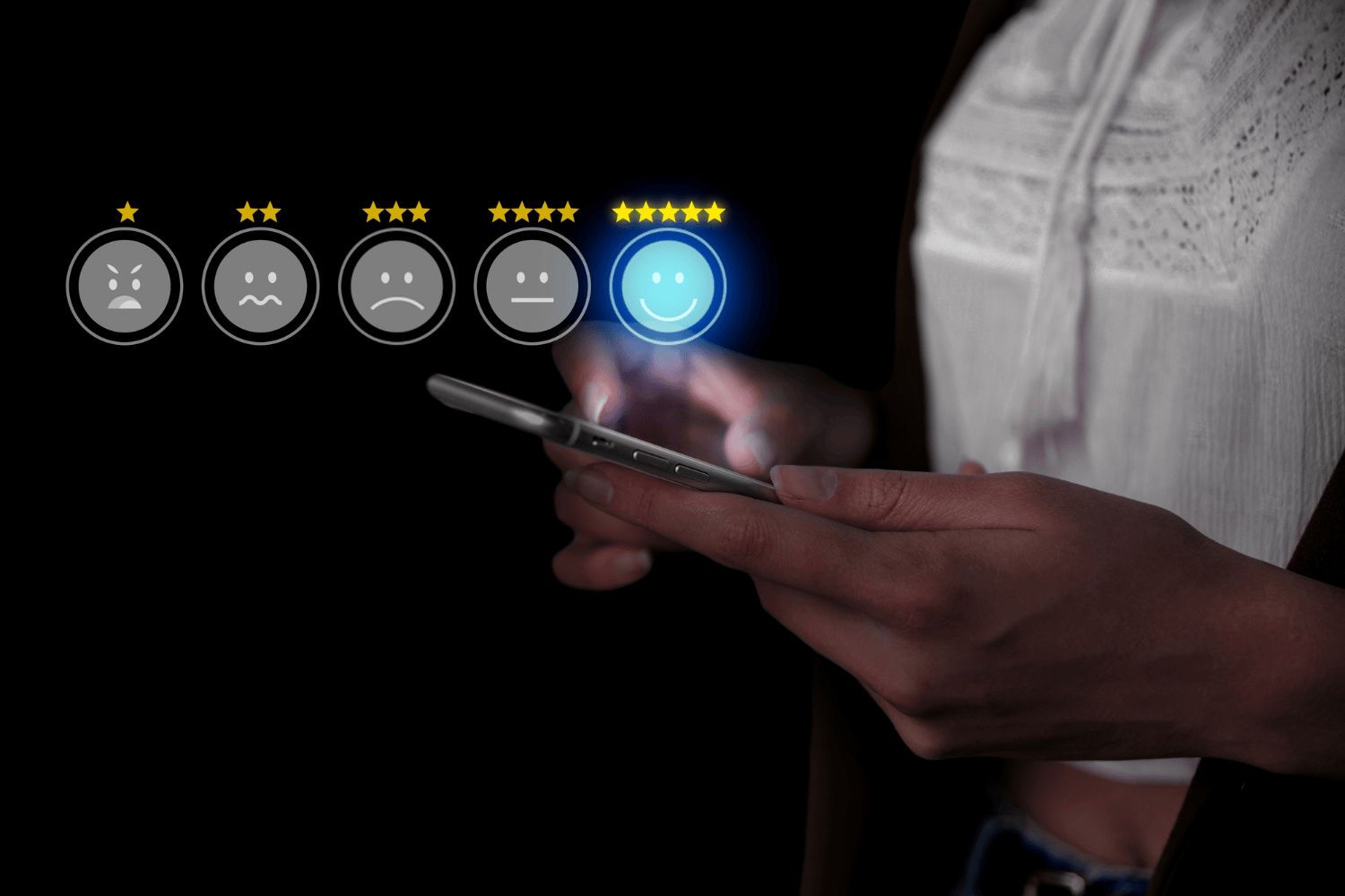 A close-up of a person gripping a cell phone with five icons of faces resembling ratings for customer satisfaction.