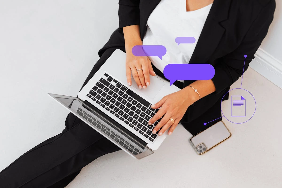 A woman dressed in a business suit sits on the floor, intently using her laptop for work.
