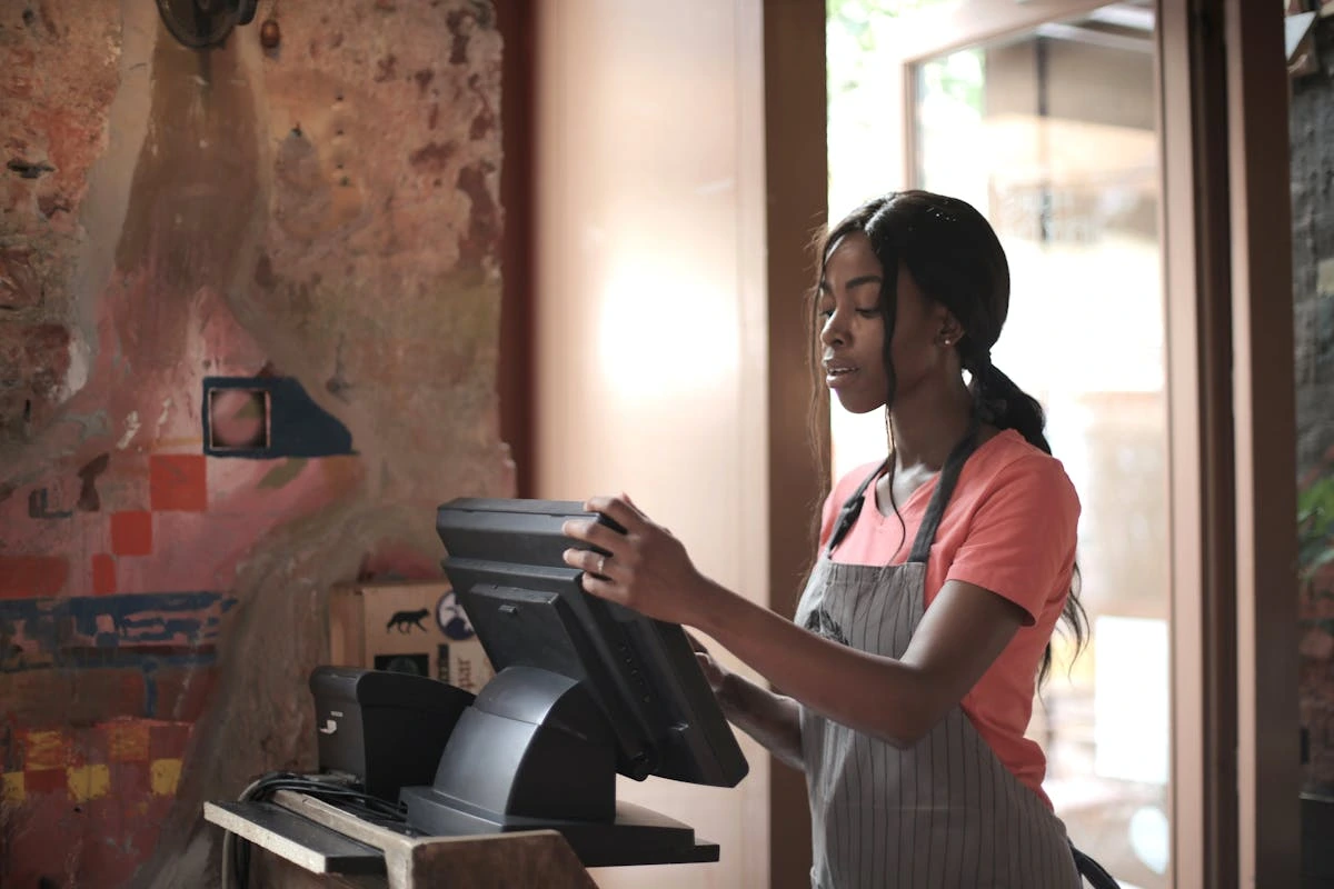 A woman wearing an apron stands in front of a computer, focused on her work or task.