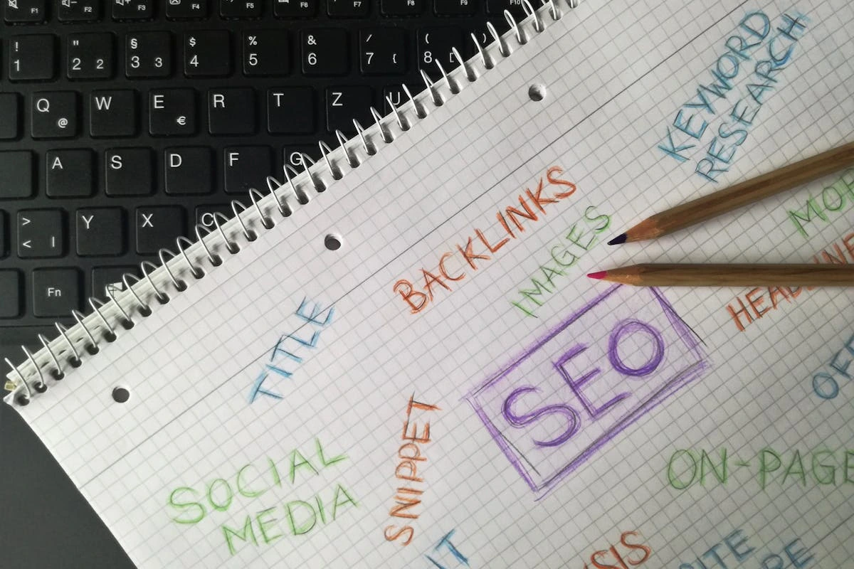 An image of a notebook over a laptop with SEO written in the middle, surrounded by key concepts around SEO.
