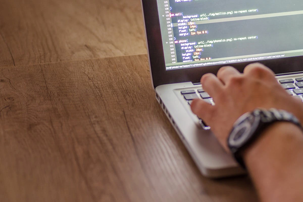 A person using a laptop, actively typing lines of code.