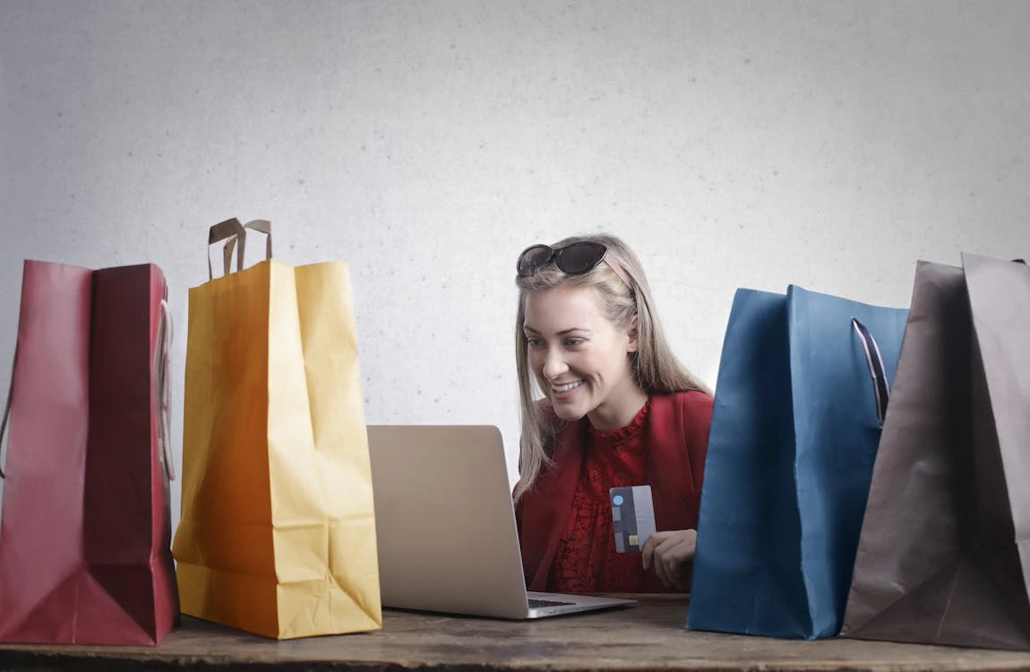 A woman sits at a table surrounded by shopping bags, smiling and enjoying her shopping experience.